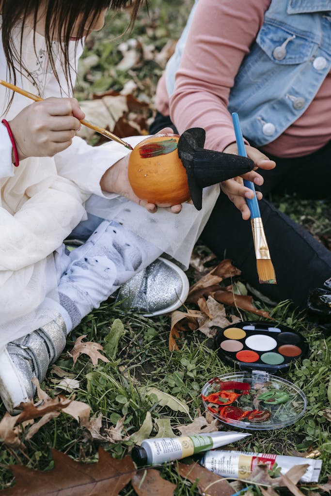 Crop faceless girls painting Halloween pumpkin in park